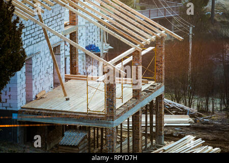 Cottage house building under construction with walls made of hollow foam insulation blocks, wooden roof frame and attached porch terrace with brick co Stock Photo