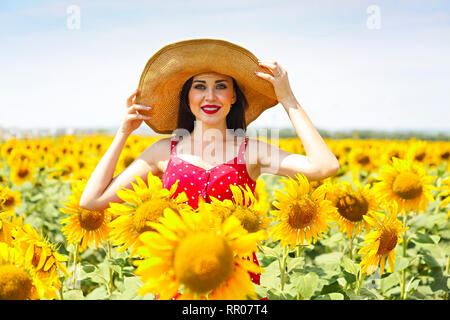 Pretty brunette woman wearing the big hat in sunflower field Stock Photo