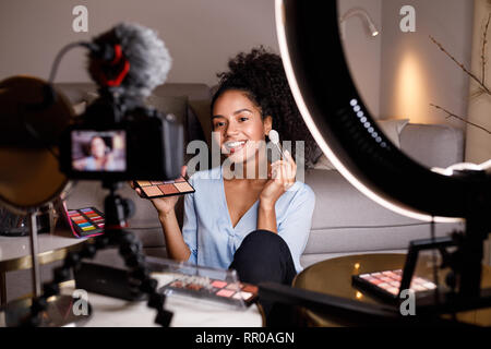 Beauty vlogger making a video tutorial on makeup in living room Stock Photo