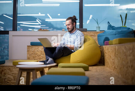 software developer writing programming code using laptop computer while sitting on lazy bag in modern startup office Stock Photo