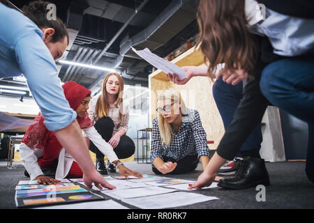 young blonde businesswoman having meeting with her multiethnic startup business team in modern office interior,presenting new ideas on the floor Stock Photo