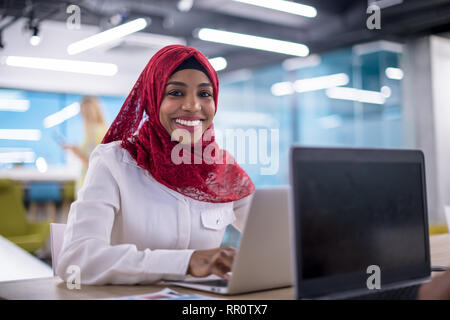 Young modern black muslim business woman wearing a red hijab,working on laptop computer in startup office. Diversity, multiracial concept Stock Photo
