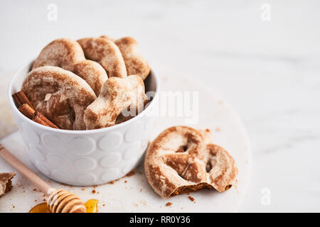 Traditional Chtristmas gingerbread cookies made of ginger, honey and cinnamon with icing in white bowl on white servig plate over white marble backgro Stock Photo