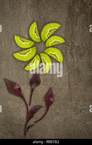 Creative flower made of Kiwis with beetroot leaves cut from below lit on a stone background Food concept Stock Photo