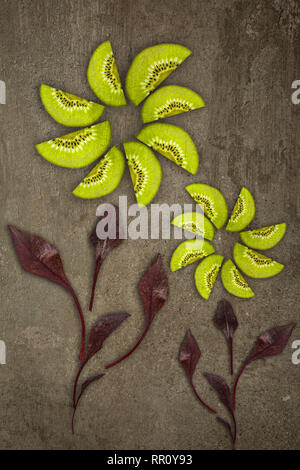 Creative flowers made of Kiwis with beetroot leaves cut from below lit on a stone background Food concept Stock Photo