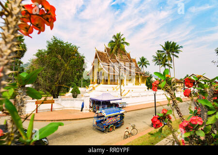 Stunning view of a tuk tuk (auto rickshaw) passing in front of the beautiful Haw Pha Bang Temple.