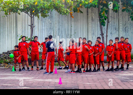 Schoolchildren in red sports uniform  their teacher playing a ball game in Jimbaran Bay Bali Indonesia. Stock Photo