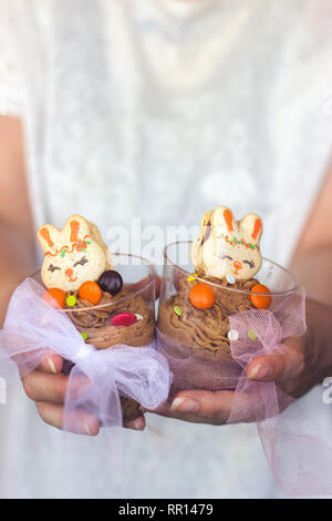 Woman's hands holding transparent plastic cup with chocolate mousse, decorated with bunny shaped cookie Stock Photo