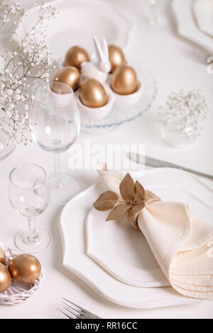 Happy Easter! Golden decor and table setting of the Easter table with white dishes of white color. Selective focus. Stock Photo