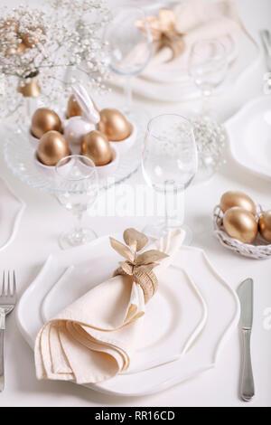 Happy Easter! Golden decor and table setting of the Easter table with white dishes of white color. Selective focus. Stock Photo