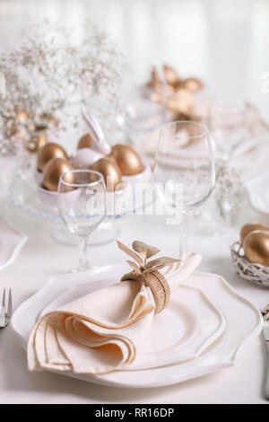 Happy Easter! Golden decor and table setting of the Easter table with white dishes of white color. Selective focus. Stock Photo