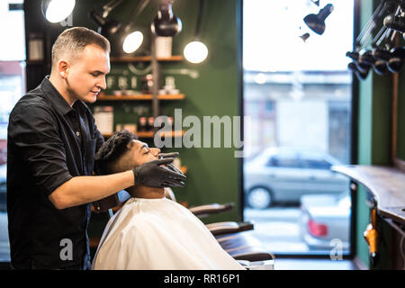 Hairstylist applying after shaving lotion in barber shop Stock Photo