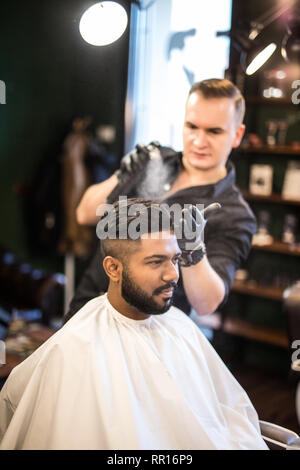 Barber combs his hair to a young guy with a beard and mustache and ...