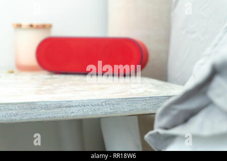 Bright red radio alarm clock and candle jar on a bedside table nightstand, with bed and linens showing in soft colors. Stock Photo