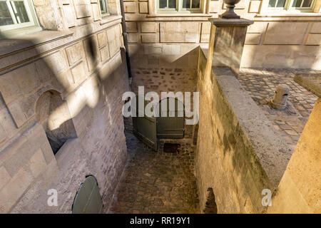 A basement area with wooden curved doors and cobbled stones  in the Courtyard of Hôtel de Sully , Paris France Stock Photo