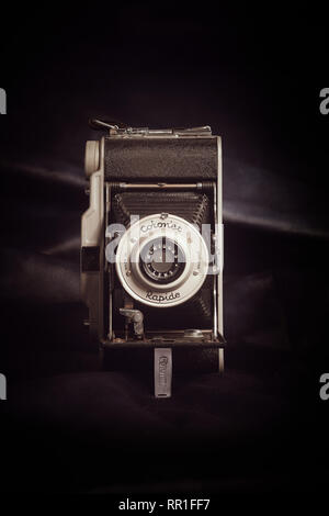 Vertical aspect front view of a vintage bellows film camera against a dark fabric background. Stock Photo