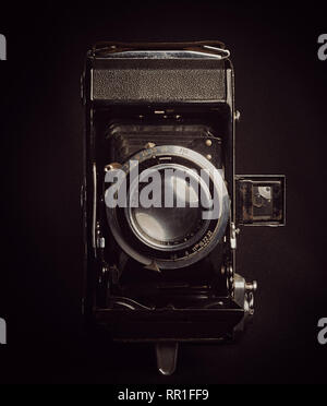 Vertical aspect front view of an unbranded vintage bellows film camera against a black background. Stock Photo