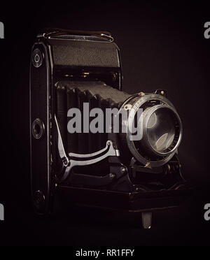 Vertical aspect right side view of an unbranded vintage bellows film camera against a black background. Stock Photo