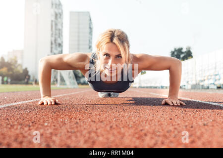 Sporty Lifestyle. Young woman on stadium doing push ups smiling happy front view Stock Photo