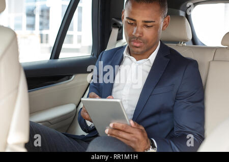 Young businessman sitting on back seat in car browsing digital tablet concentrated Stock Photo