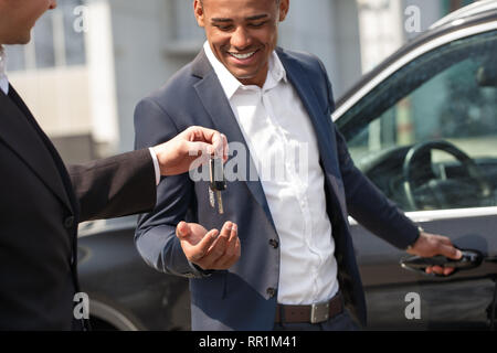 Agent giving keys to young man opening door standing near car happy Stock Photo