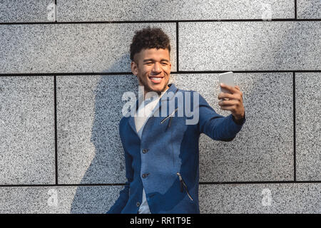 Freestyle. Mulatto guy standing isolated on wall taking selfie on smartphone cheerful Stock Photo