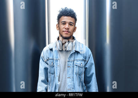 Outdoors Leisure. Mulatto guy with headphones around neck standing on city street smiling joyful Stock Photo