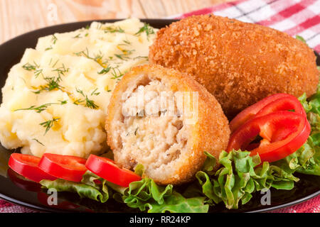 two fried breaded cutlet with mashed potatoes and lettuce on a black plate wooden background Stock Photo