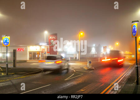 Neon signs & Car Light Trails in Southport, Merseyside. Hazy, foggy, misty start to the day with light drizzle as busy early morning city centre traffic lights up the damp pavements. Traffic car headlights and tail lights from late night revellers using homebound taxis;  Lights from passing vehicles leave reflections on the road surface. Stock Photo