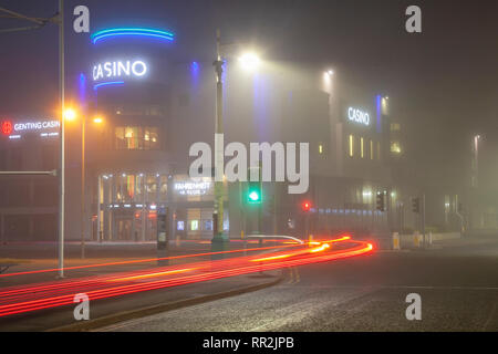 British Casino & Hotel complex & Car Light Trails in Southport, Merseyside. Hazy, foggy, misty start to the day with light drizzle as early morning city centre traffic lights up the damp pavements. Traffic car headlights and tail lights from late night revellers using homebound taxis;  Lights from passing vehicles leave reflections on the road surface. Credit: MWI/AlamyLiveNews.