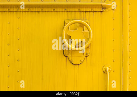 industrial valve wheel on yellow painted metal wall surface. grunge weathered background Stock Photo