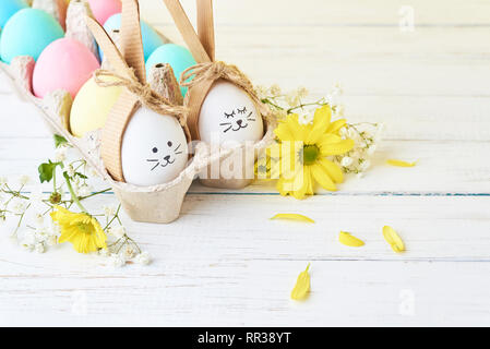 Easter colored eggs with painted faces in paper tray with decorationd on white background Stock Photo