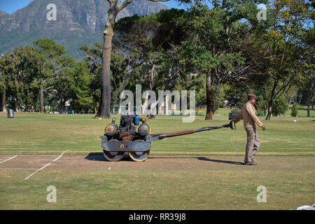 Groundskeeper using a vintage roller to harden to surface of the bowling lane of the local park's cricket ground.  Close up view of machine and man. Stock Photo