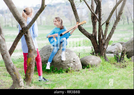 music concept of two young caucasian girls playing guitar and singing songs together spring park Stock Photo