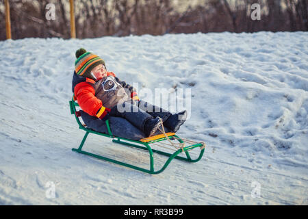 Boy enjoying a sleigh ride. Children riding a sledge. Child play outdoors in snow. Kids sled in winter park. Stock Photo