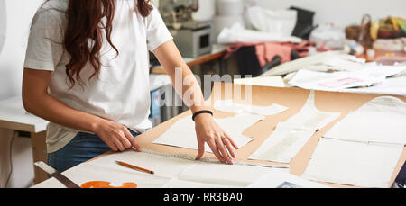 Workplace in design studio. Professional female designer making paper patterns using measuring tape, ruler and curve on blurred background of tailor atelier. Exclusive clothes making concept. Stock Photo