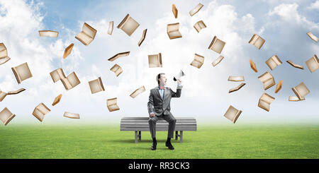 Young businessman sitting on bench and screaming emotionally in megaphone Stock Photo