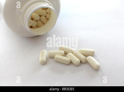 A close up photograph of medication, white tablets spilling from their bottle onto a white surface. Healthcare, illness concept Stock Photo