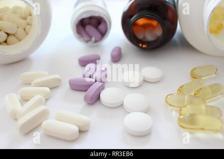 A close up photograph of a variety of medication, tablets and pills spilling from their bottles onto a white surface. Healthcare, illness concept Stock Photo