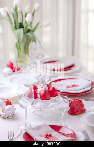 Happy easter. Decor and table setting of the Easter table is a vase with white tulips and dishes of red and white color. Easter colored eggs with whit Stock Photo