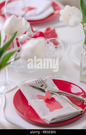 Happy easter. Decor and table setting of the Easter table is a vase with white tulips and dishes of red and white color. Easter colored eggs with whit Stock Photo