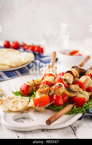 Chicken kebabs on skewers with mushrooms, bell peppers, onions. Barbecue tomato sauce and fresh pitas in the background. Copyspace. Stock Photo
