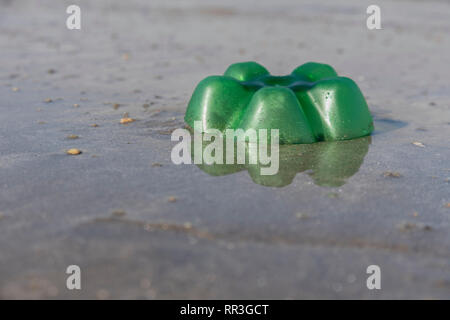 Empty plastic soft drink bottle left embedded in silty sand of beach. For plastic beach pollution, ocean polluting plastic, plastic bottles UK beach. Stock Photo