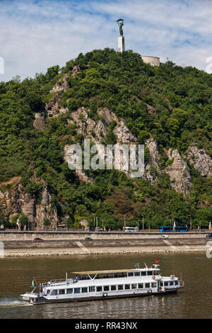 Gellert Hill by the Danube river and passenger boat on a cruise in city of Budapest, Hungary Stock Photo