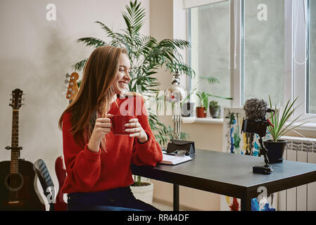 Successful blogger. Side view of smiling female blogger drinking a tea while making a new video at home. Social Media. Blog. Youtube Stock Photo