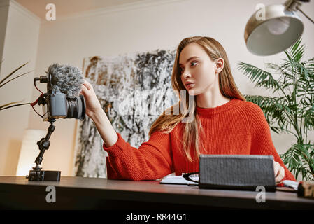 One minute...Portrait of female blogger setting up her tripod mounted digital camera while making a new video at home. Social Media. Blog. Youtube Stock Photo