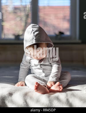 Happy baby boy in grey pyjamas on bed in his room Stock Photo