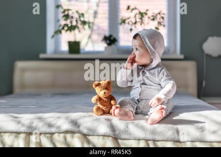Happy baby boy in grey pyjamas on bed in his room Stock Photo