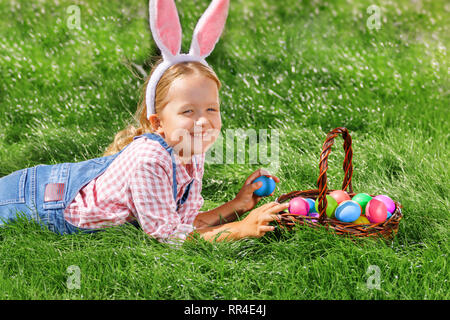 Cute little girl child with basket on green grass in the park. Easter Egg Hunting Concept Stock Photo