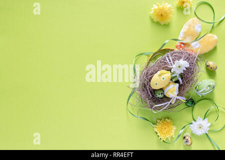 Colourful Easter eggs in birds nest with festive decoration on green background, top view- image Stock Photo